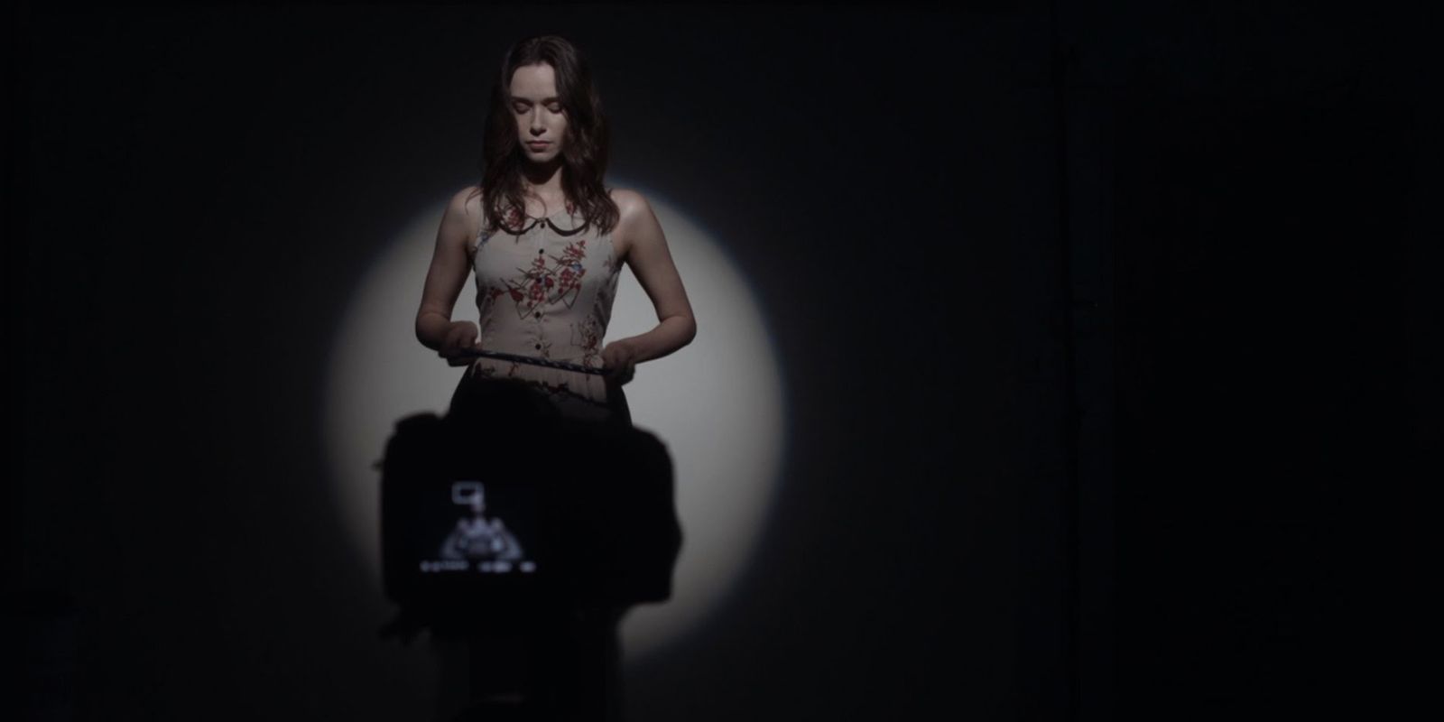 A woman stands in front of a camera in a dimly lit audition room
