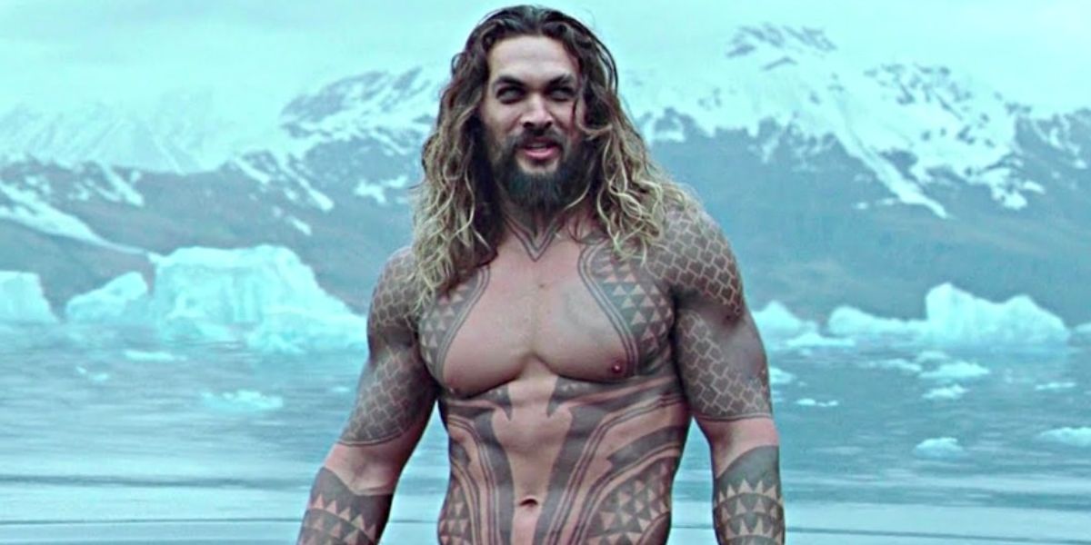 Jason Momoa as Aquaman standing shirtless in the water in front of the mountains.