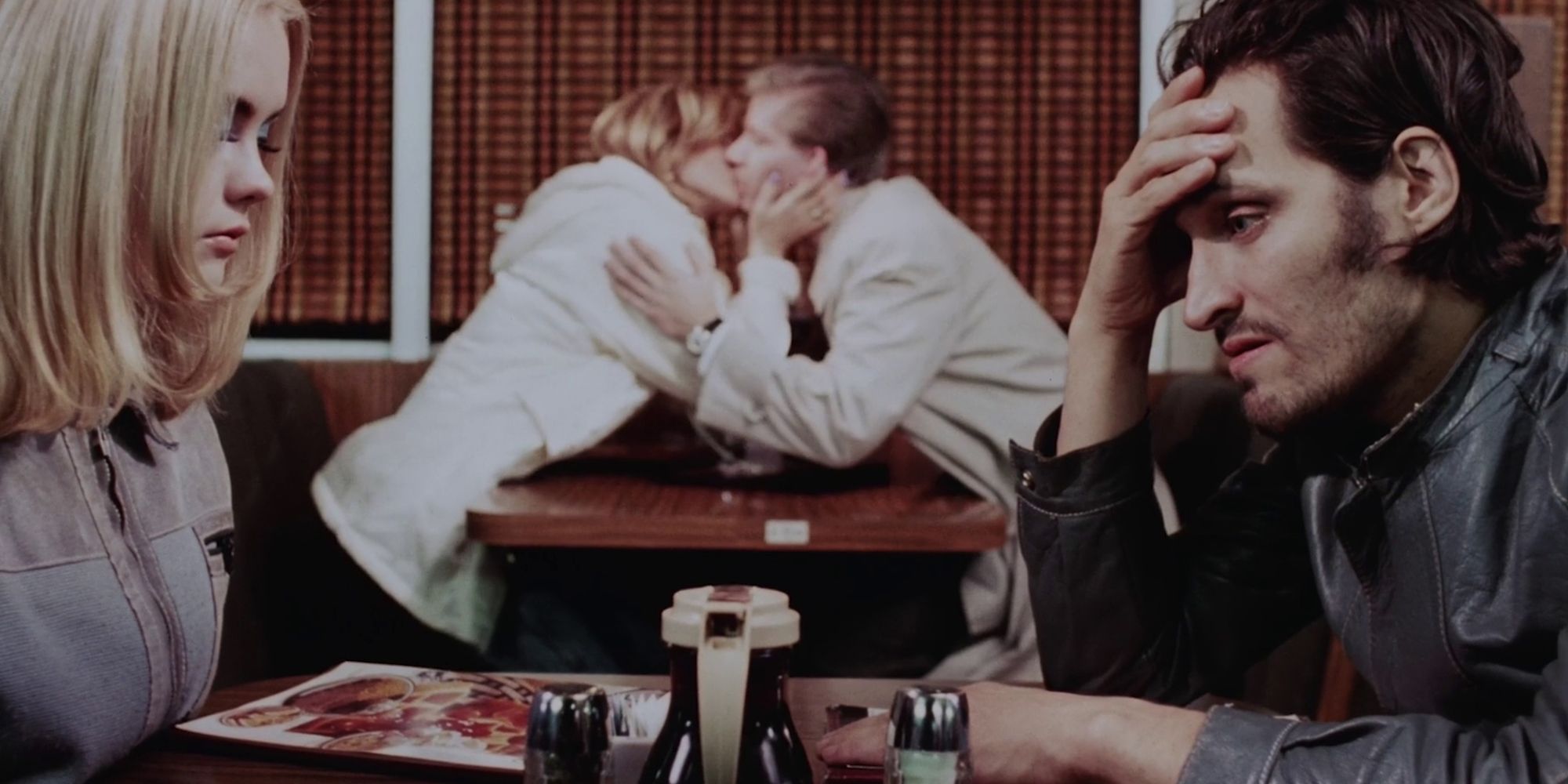 Buffalo '66 Vincent Gallo e Christina Ricci sentados à mesa de um restaurante enquanto um casal se beija ao fundo