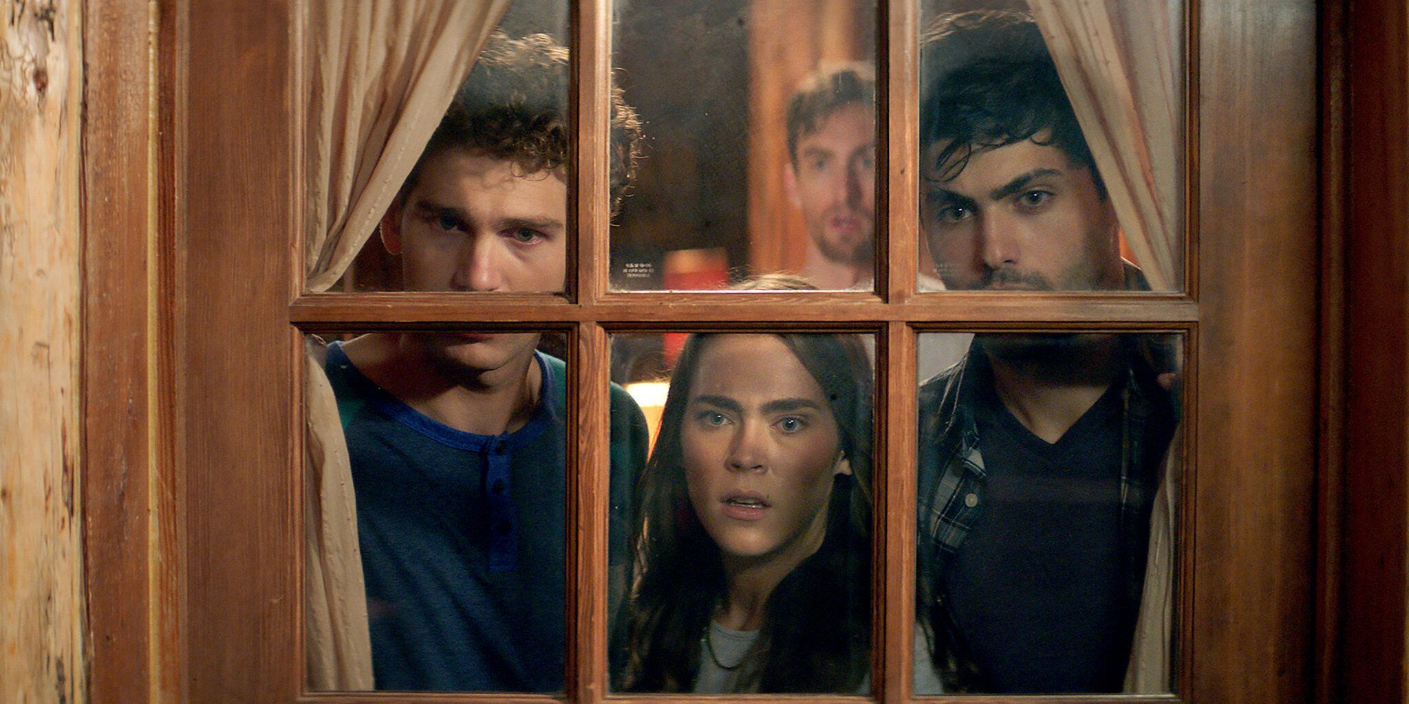 A still from the 2016 remake of Cabin Fever in which a cast of characters is looking outside the window of the cabin in fear and dismay 