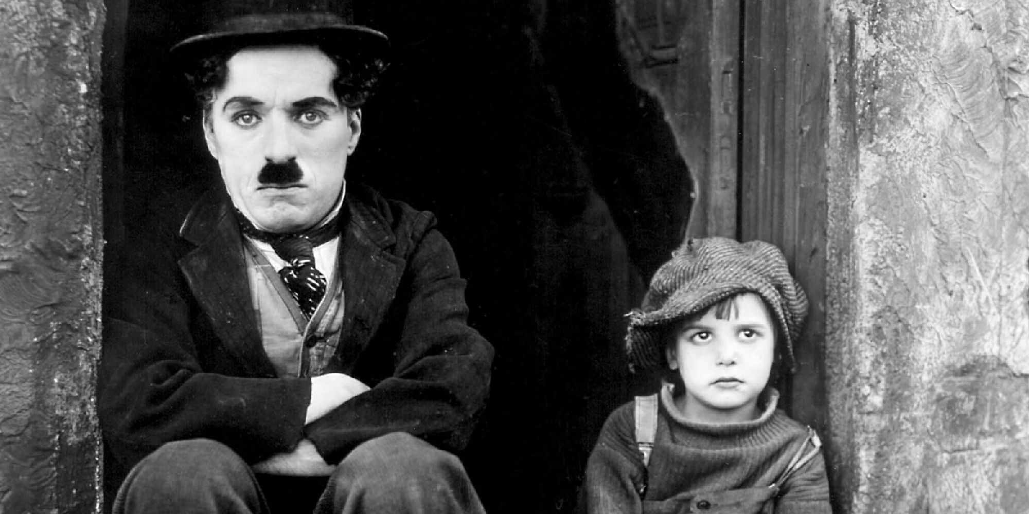Charlie Chaplin and Jackie Coogan as The Tramp and the Kid sitting on a door steep looking at the camera in The Kid