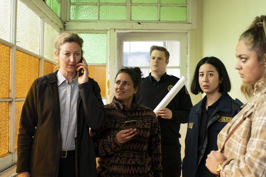 deadloch group of people looking at woman on phone in police station