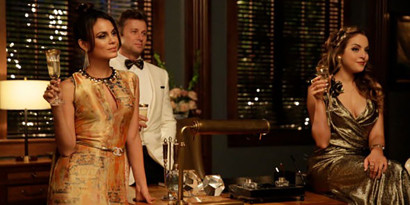 Crystal and Fallon holding champagne glasses, Blake behind them in a white suit jacket and bowtie in a scene from Dynasty.