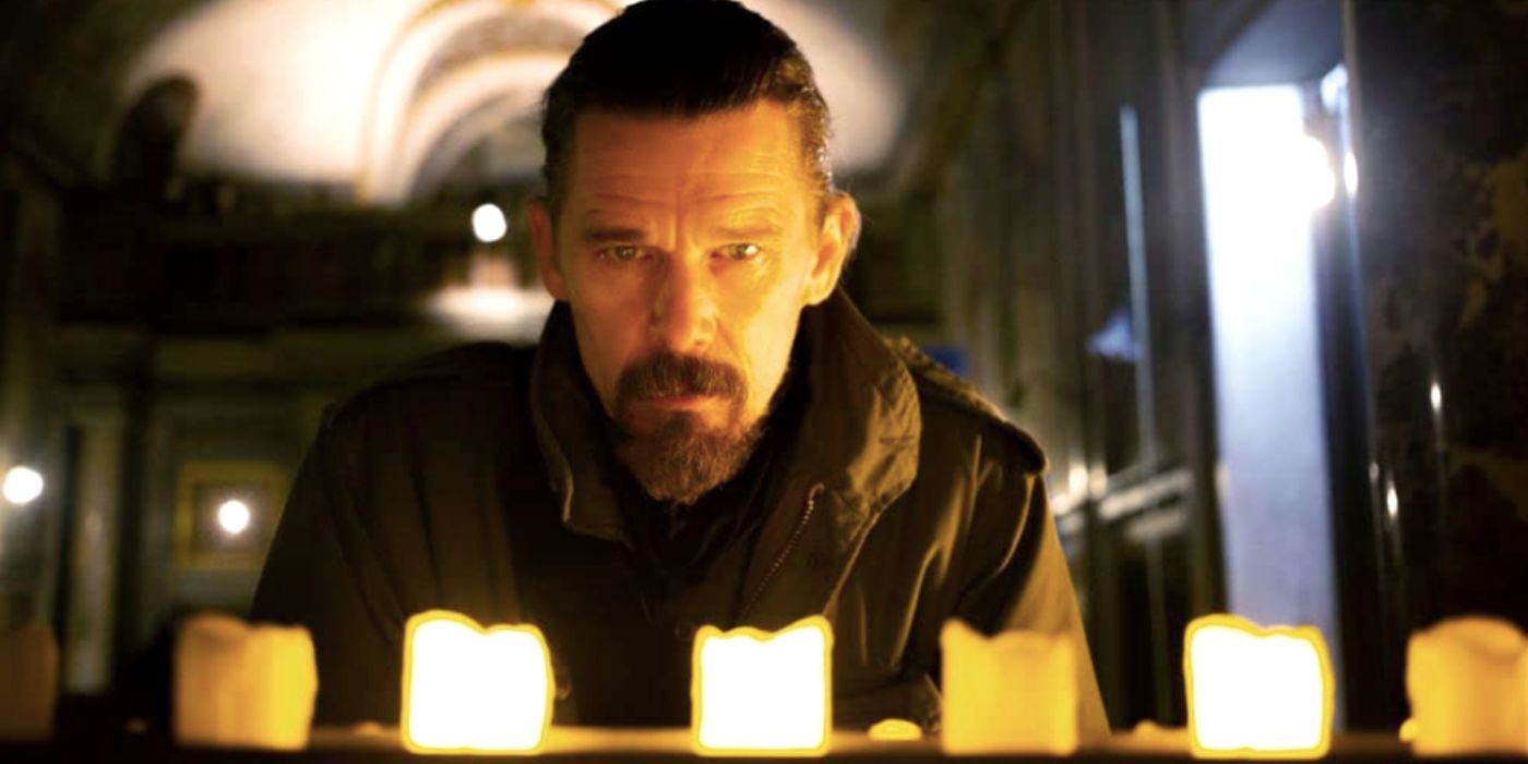 Ethan Hawke behind a row of lit candles in Zeros and Ones