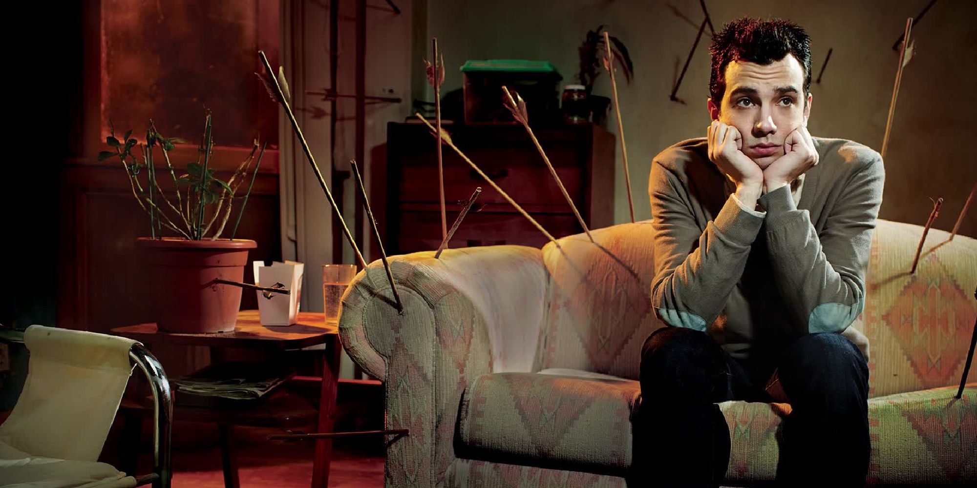 Josh sits on a couch surrounded by missed arrows in Man Seeking Woman.