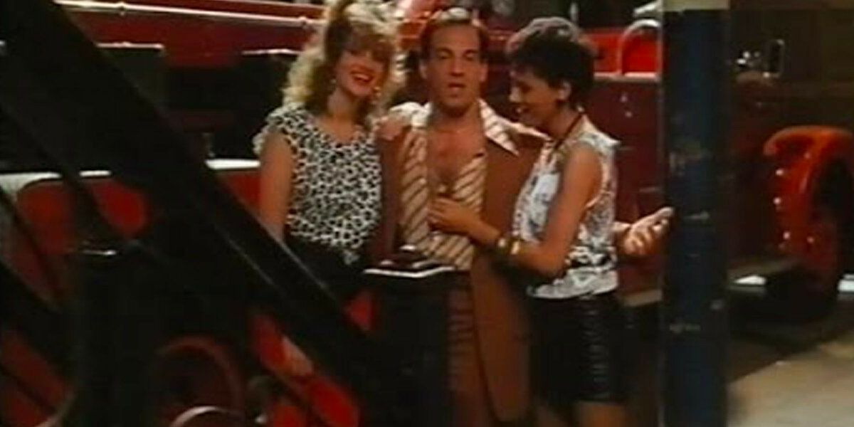 A sleazy man stands in front of a firetruck with two women in 1987 sex comedy 'Firehouse'.