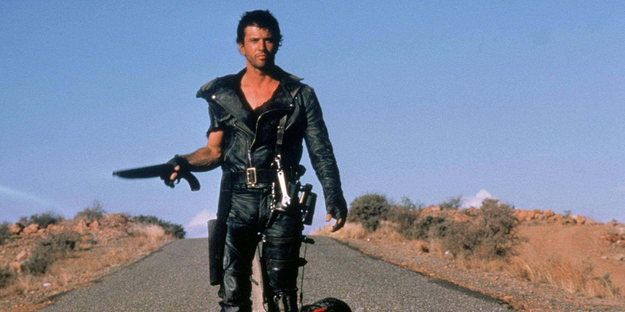 Max Rockatansky walking down a lonely highway holding a gun in Mad Max 2- The Road Warrior’