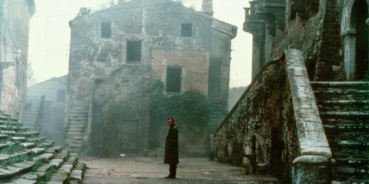 A lone poet stands in a baron, stone town amid an eerie mist. 