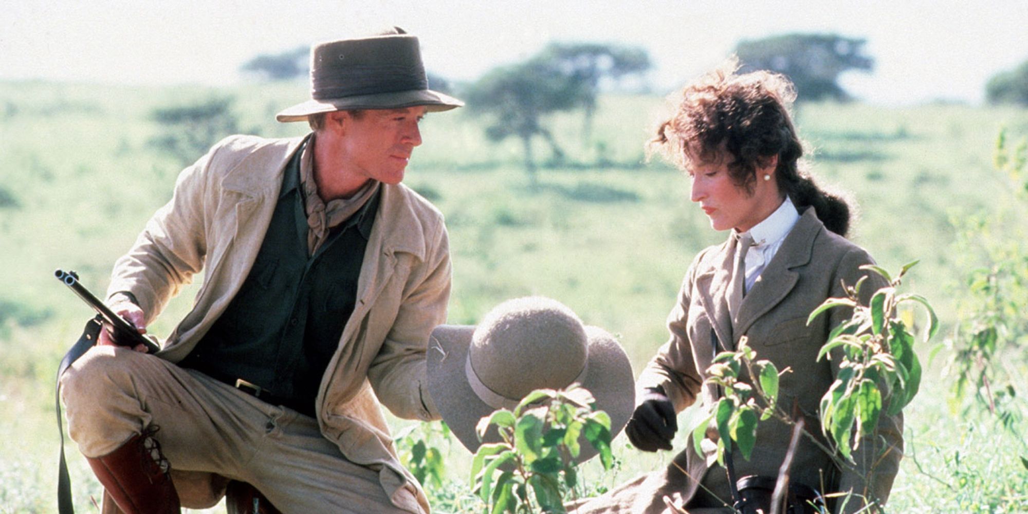 Karen (Meryl Streep) & Denys (Robert Redford) sit in a field while Denys hands Karen a hat in Out of Africa