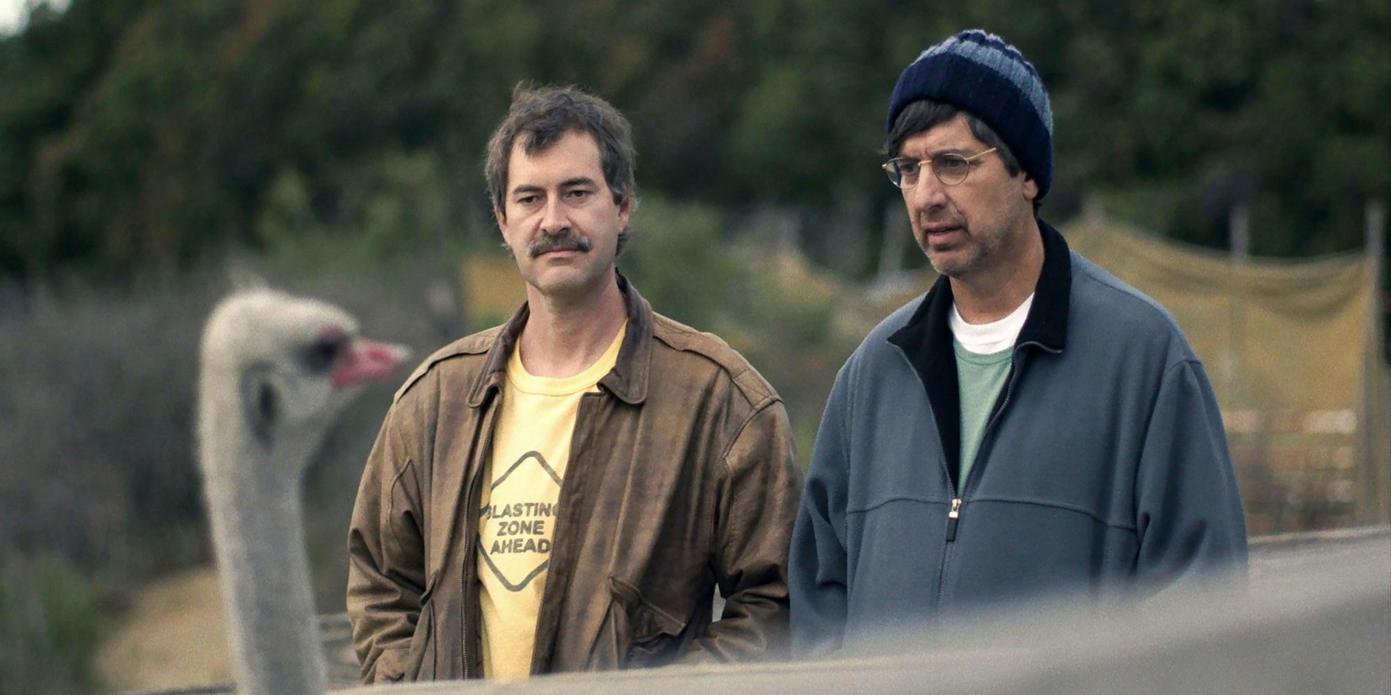Mark Duplass and Ray Romano standing near an ostrich in Paddleton.