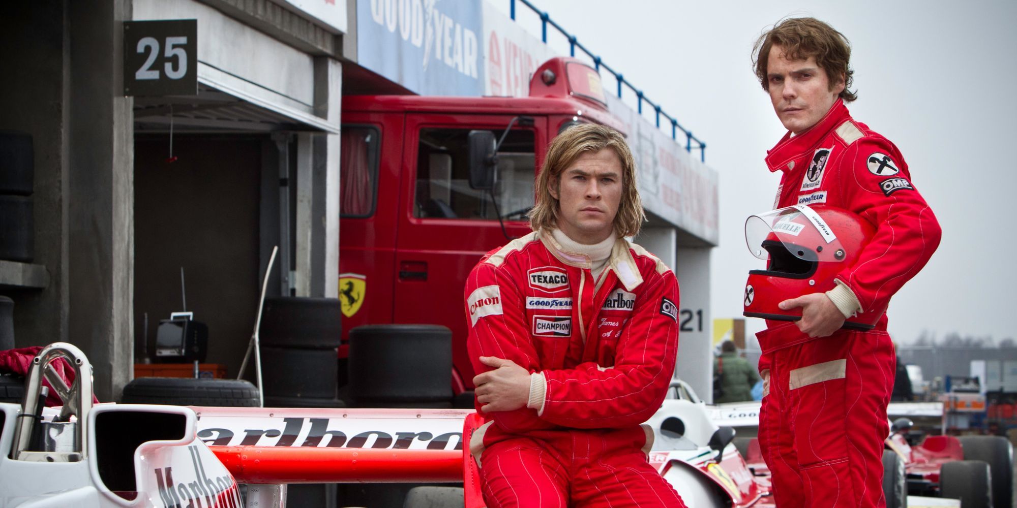 Chris Hemsworth and Daniel Brühl as James Hunt and Niki Lauda posing next to a racing car and looking directly to the camera in the film Rush