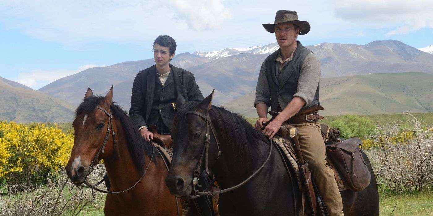 Kodi Smit-McPhee as Jay and Michael Fassbender as Jay and Silas on horseback looking ahead while on an open field in the film Slow West.