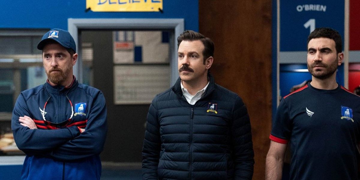 Coach Beard (Brendan Hunt), Ted Lasso (Jason Sudeikis), and Roy Kent (Brett Goldstein) standing together in the locker room at 'Ted Lasso'