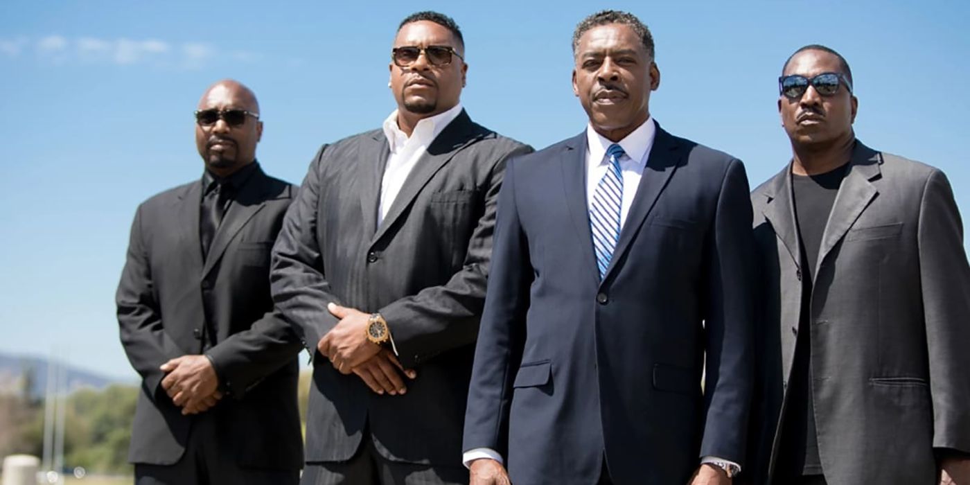 Four male characters from The Family Business standing in suits with sunglasses.
