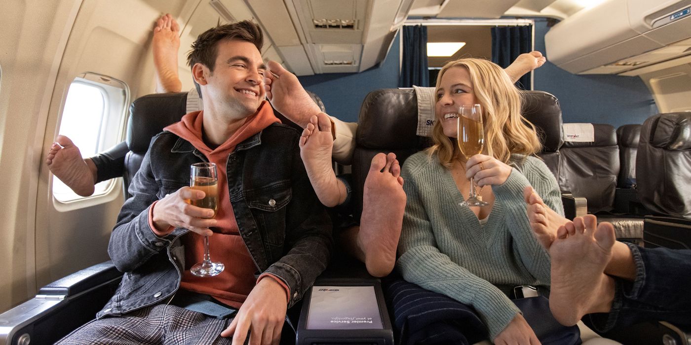Drew Tarver and Heléne Yorke are surrounded by feet on a plane in a scene from The Other Two