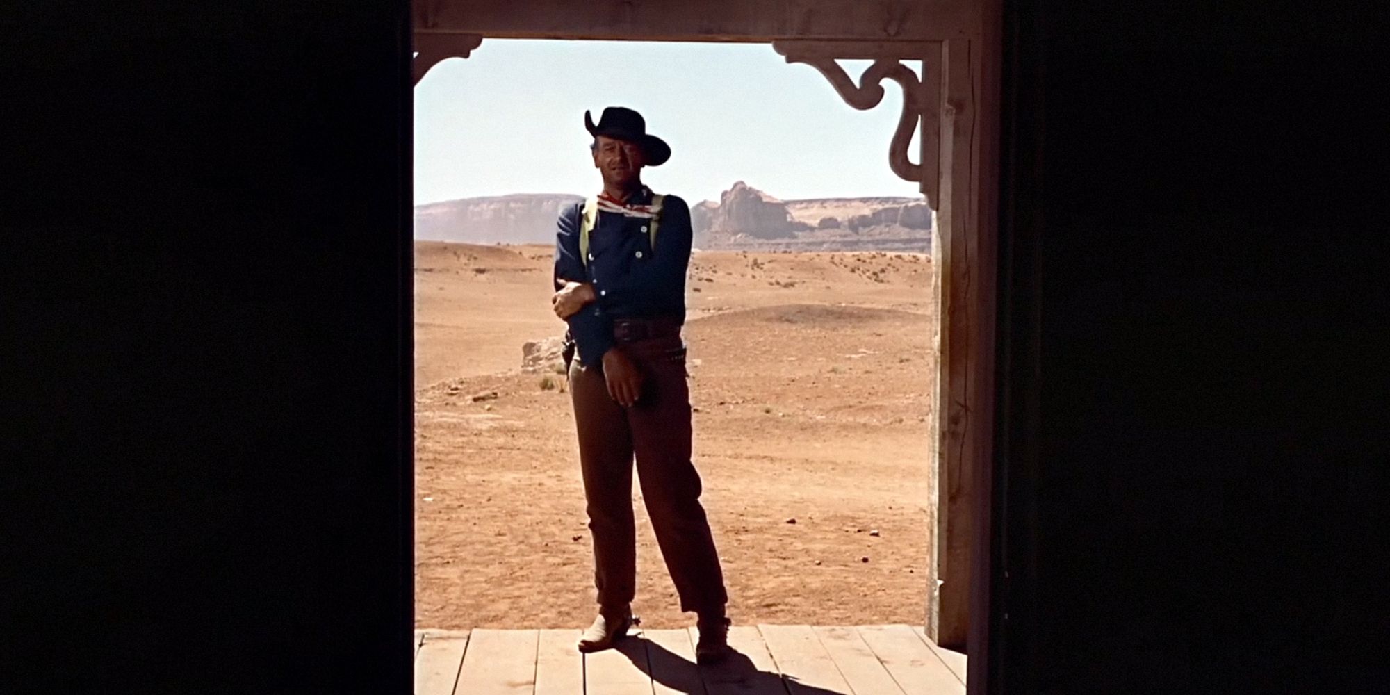 John Wayne as Ethan Edwards standing outside of a doorway in The Searchers