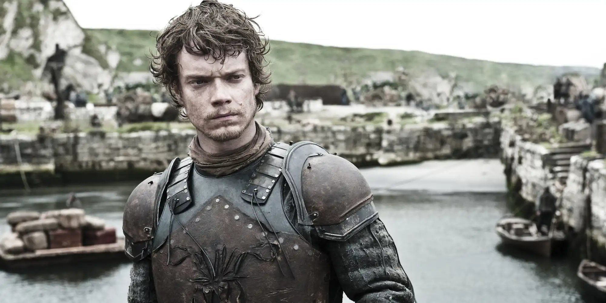 Alfie Allen as Theon Greyjoy standing in a shore looking serious in Game of Thrones.