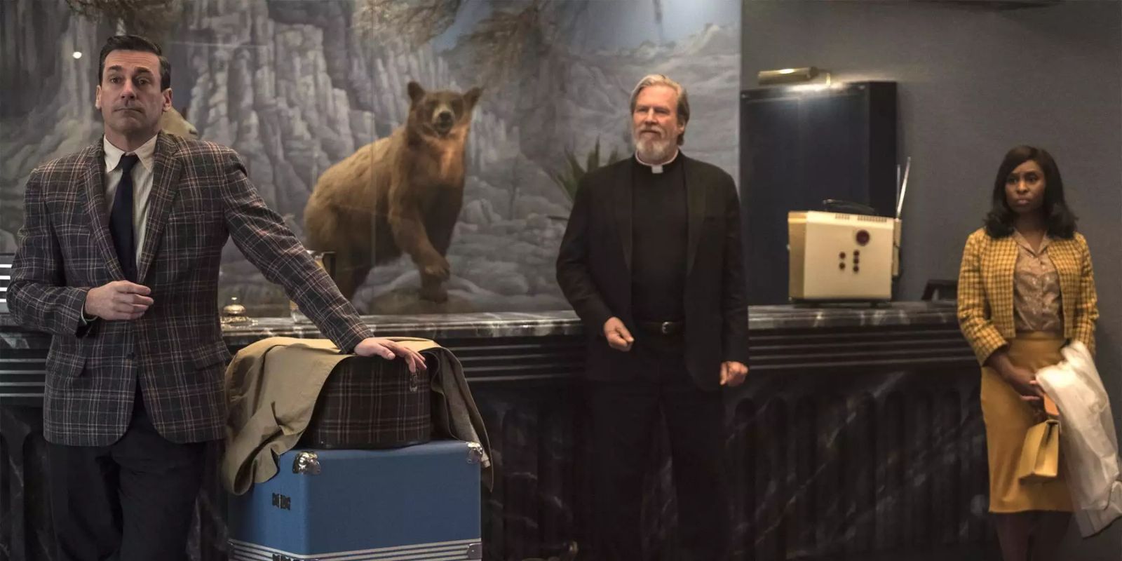 Jon Hamm, Jeff Bridges and Cynthia Erivo stand in the lobby of the El Royale with their luggage in the film Bad Times at the El Royale