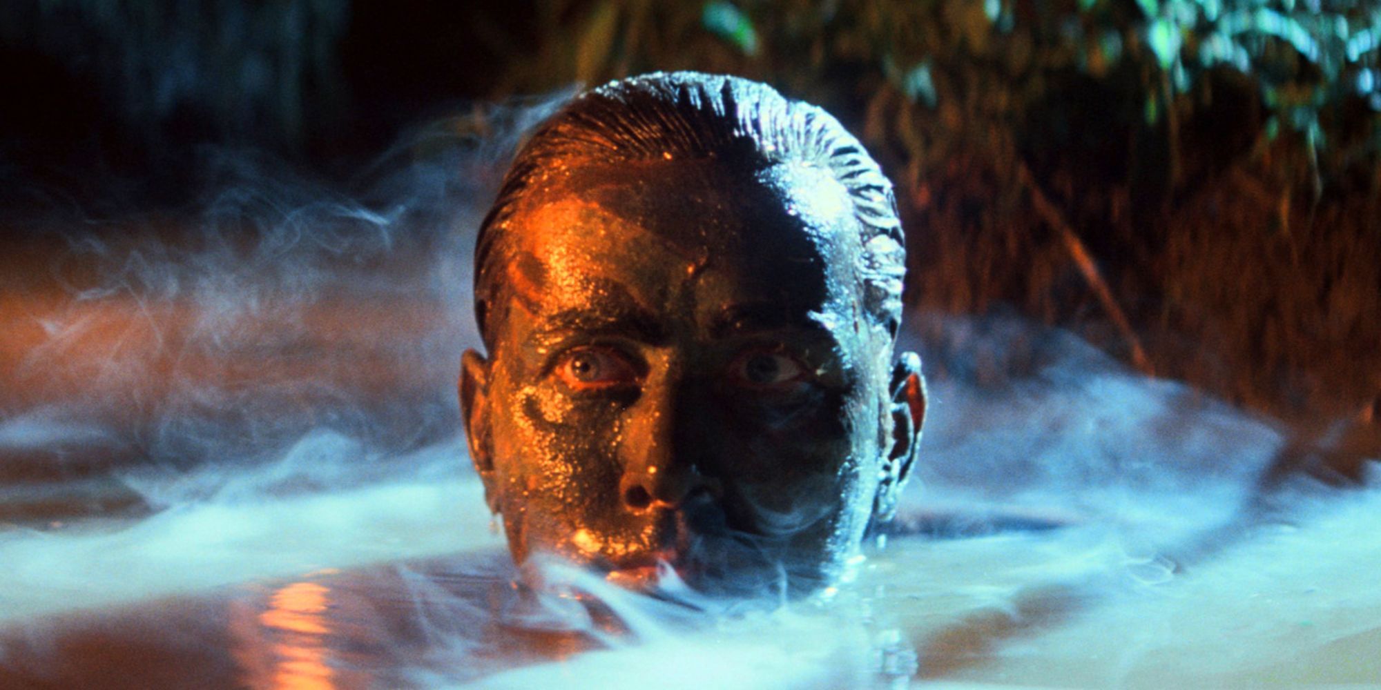 A man with camouflage paint on his face pokes his head out of the steaming water.