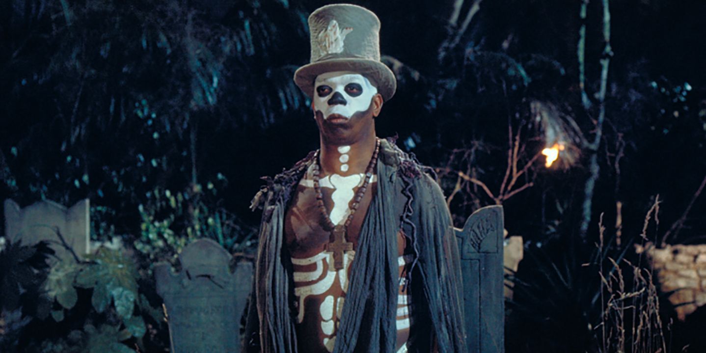 Baron Samedi adorned in voodoo skeleton paint and a top hat stands before a graveyard in 'Live and Let Die'