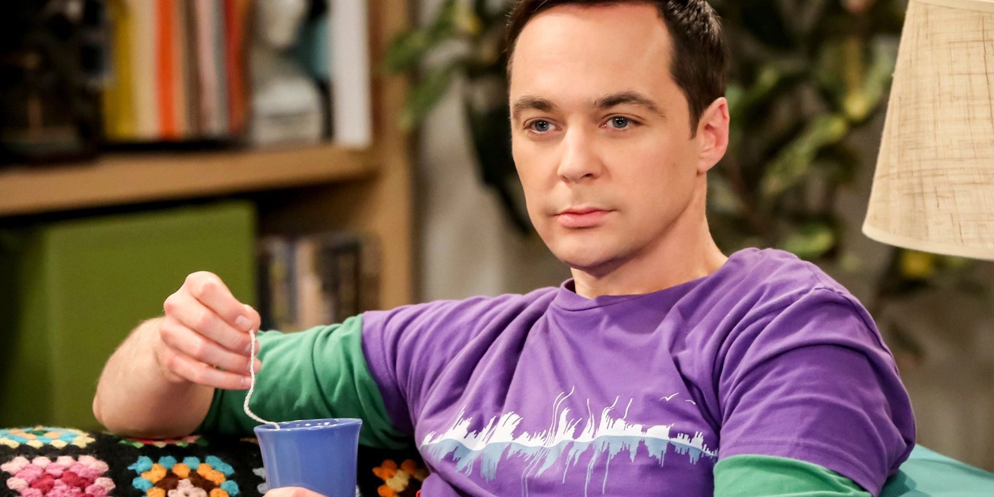 Sheldon is sitting on the couch drinking a hot drink