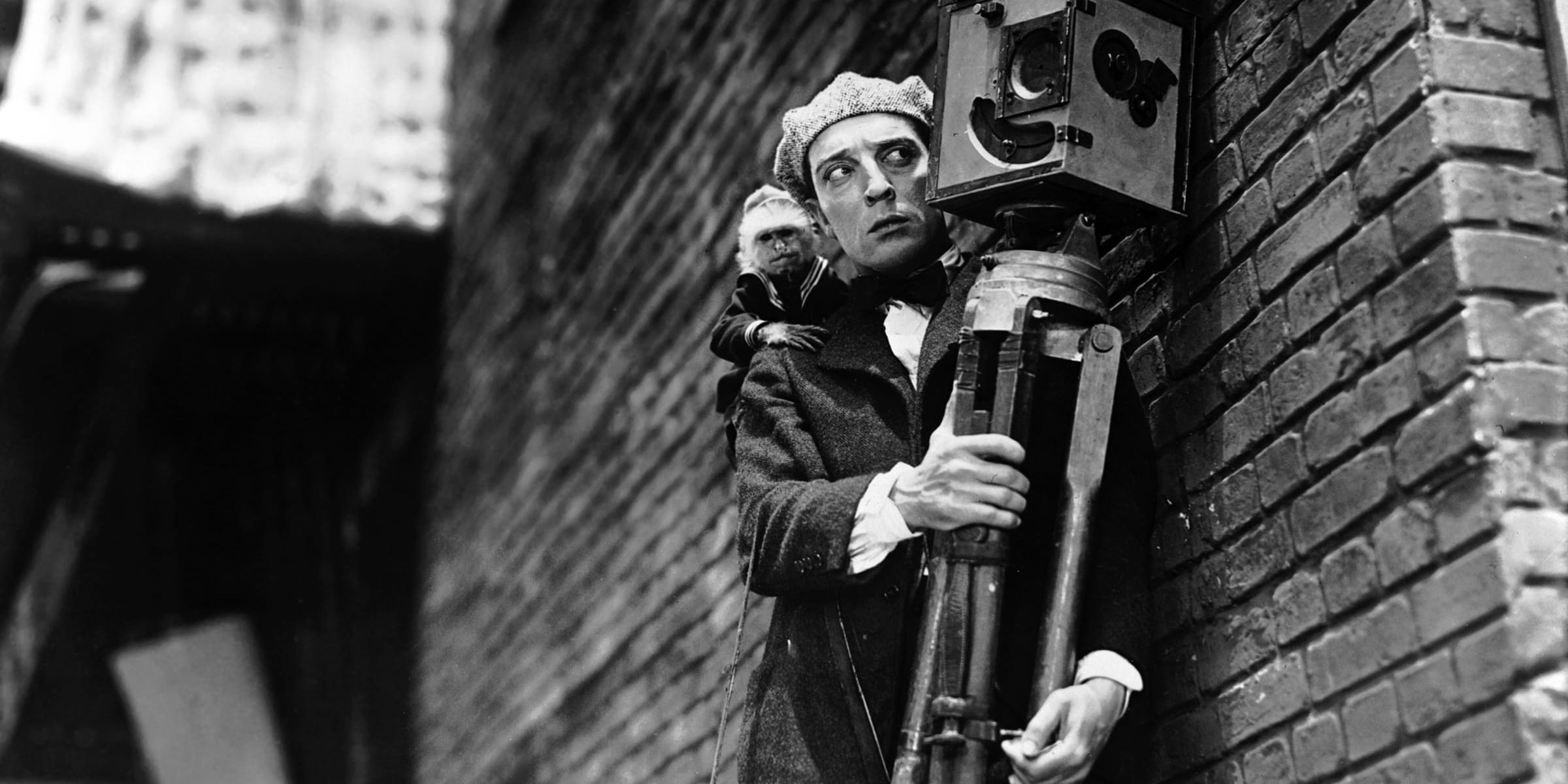 Buster Keaton as Buster holding a camera and looking intently with Josephine the Monkey on his shoulder in The Cameraman