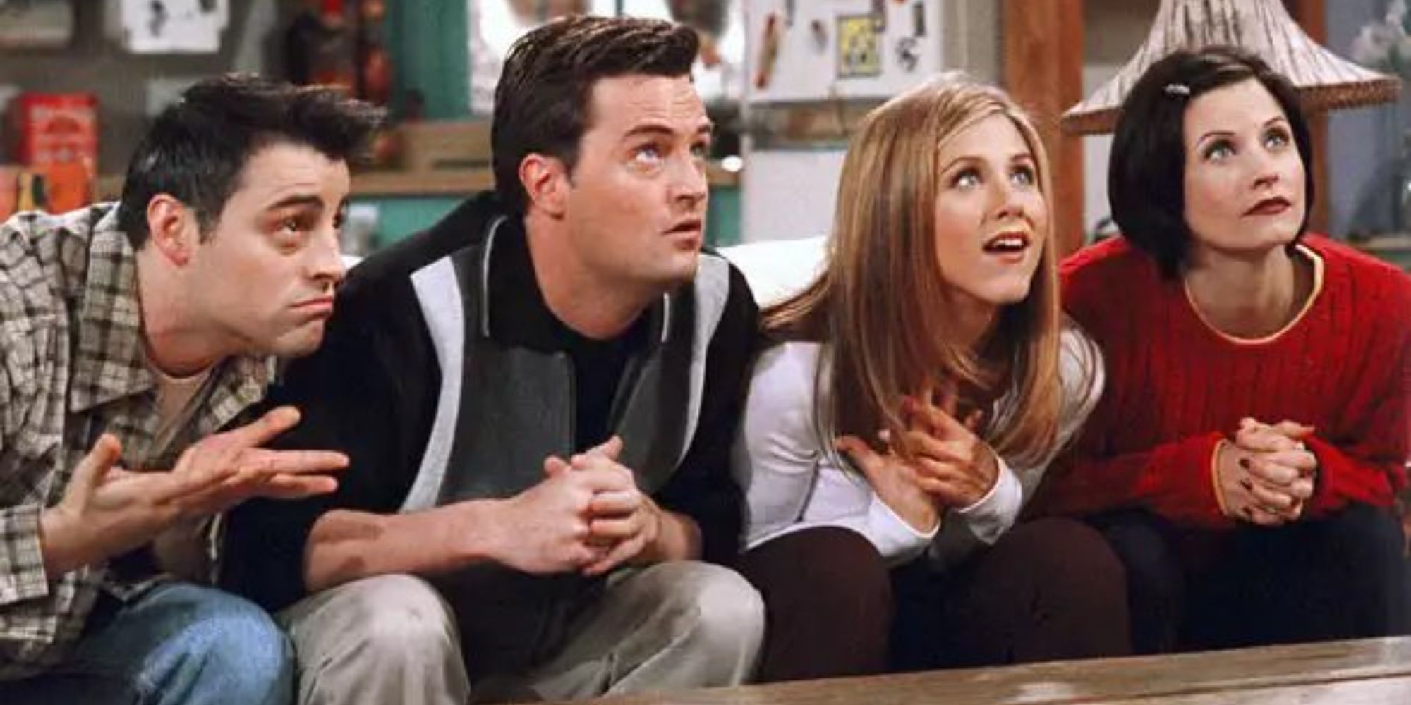 Joey (Matt LeBlanc), Chandler (Matthew Perry), Rachel (Jennifer Aniston), and Monica (Courteney Cox) sitting on the couch looking up expectantly in Frineds