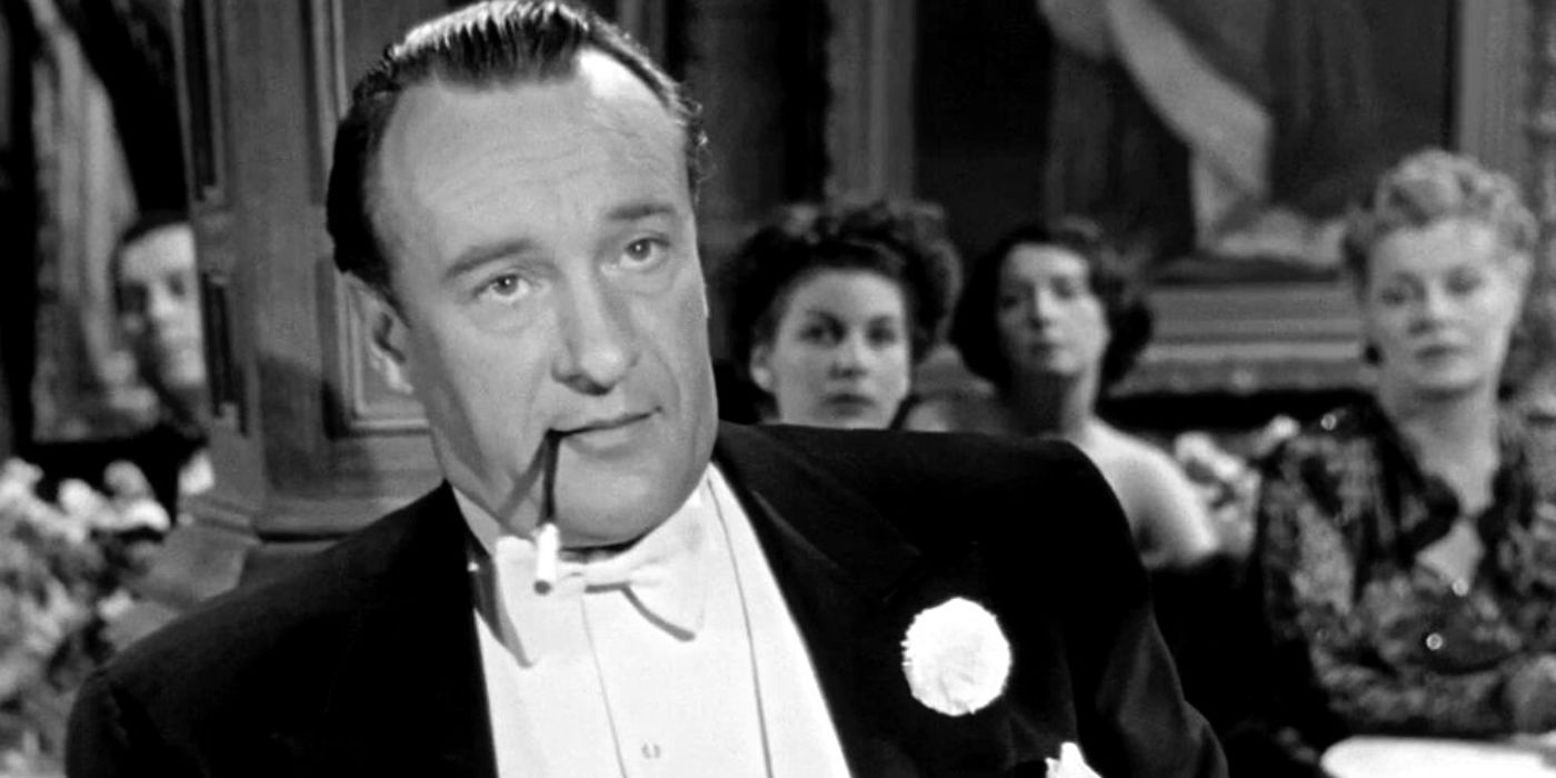 George Sanders fumant une cigarette à une table lors d'un événement dans All About Eve (1950)