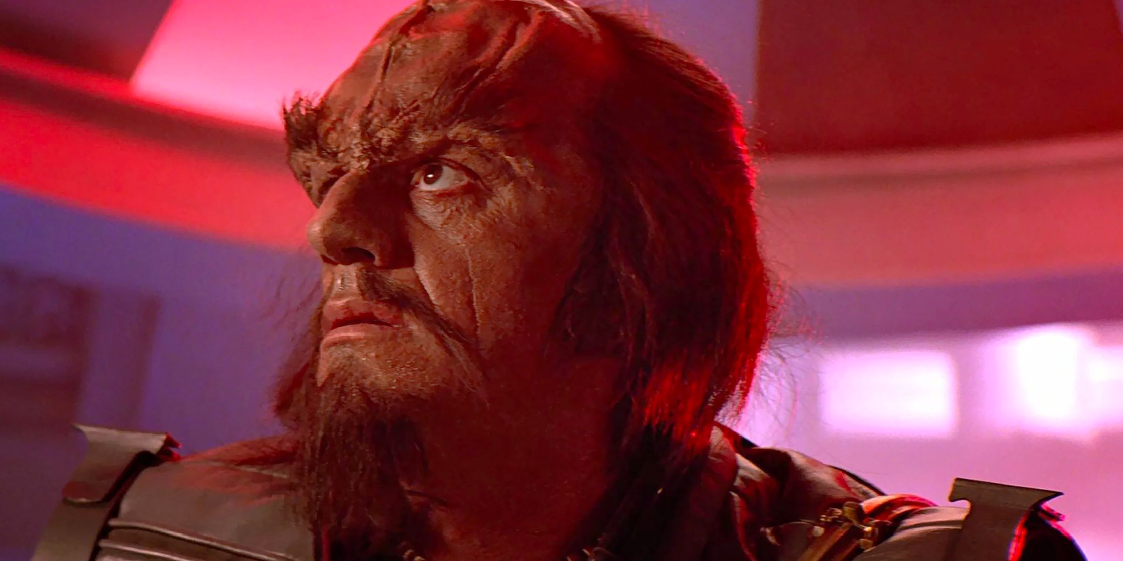 Kruge (Christopher Lloyd), a Klingon mercenary, stands aboard a ship adorned in red light. 