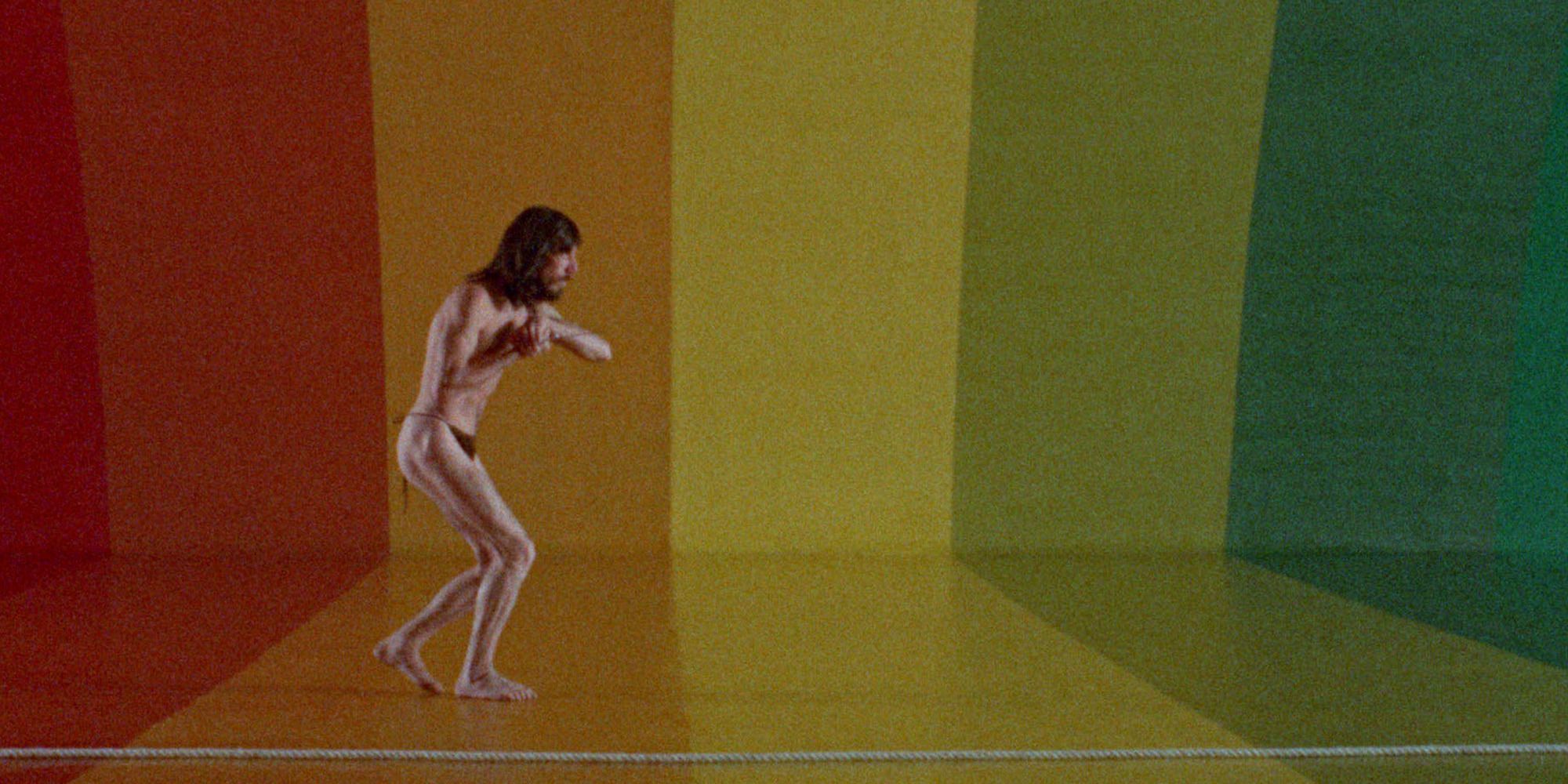 A naked man walking in a color painted with the rainbow's color in 'The Holy Mountain'