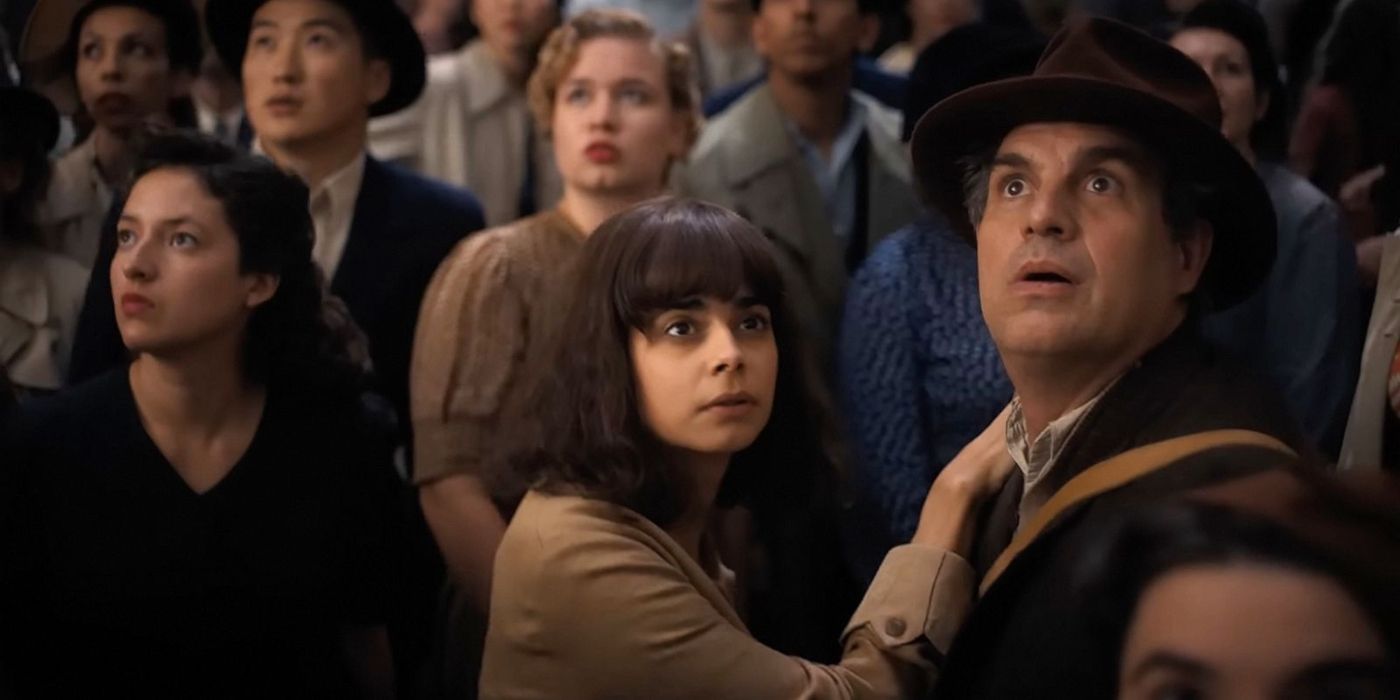 Aria Mia Loberti and Mark Ruffalo stand in a crowd looking up at the sky in 'All the Light We Cannot See.'