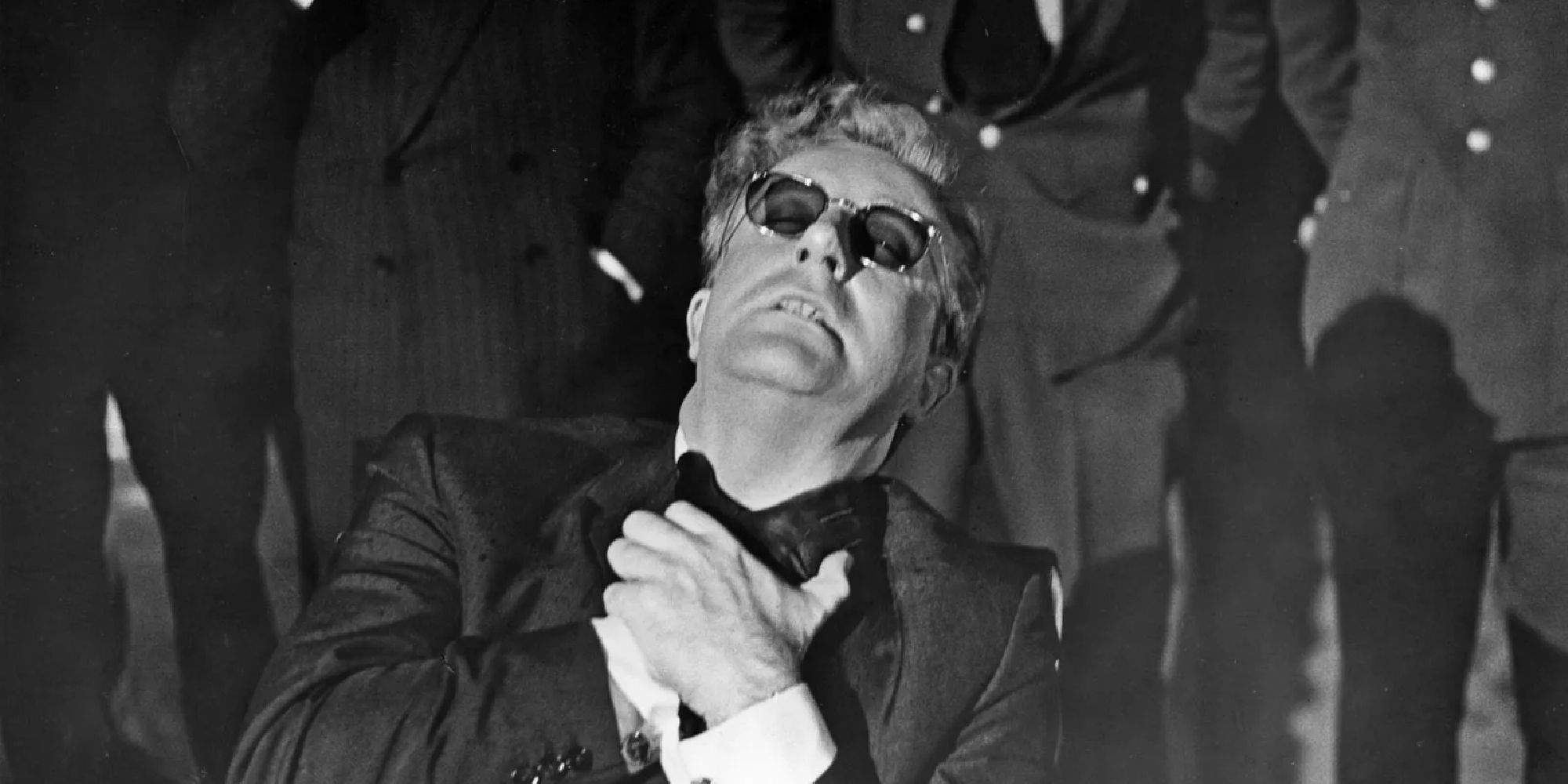 Peter Sellers as Dr. Strangelove dramatically clutching his throat with both hands in Dr. Strangelove