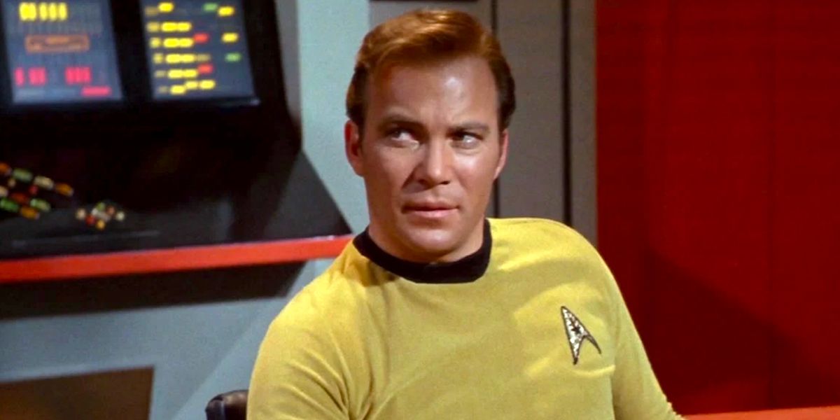 Captain Kirk (William Shatner) adorned in his yellow shirt sits at the helm of the USS Enterprise.