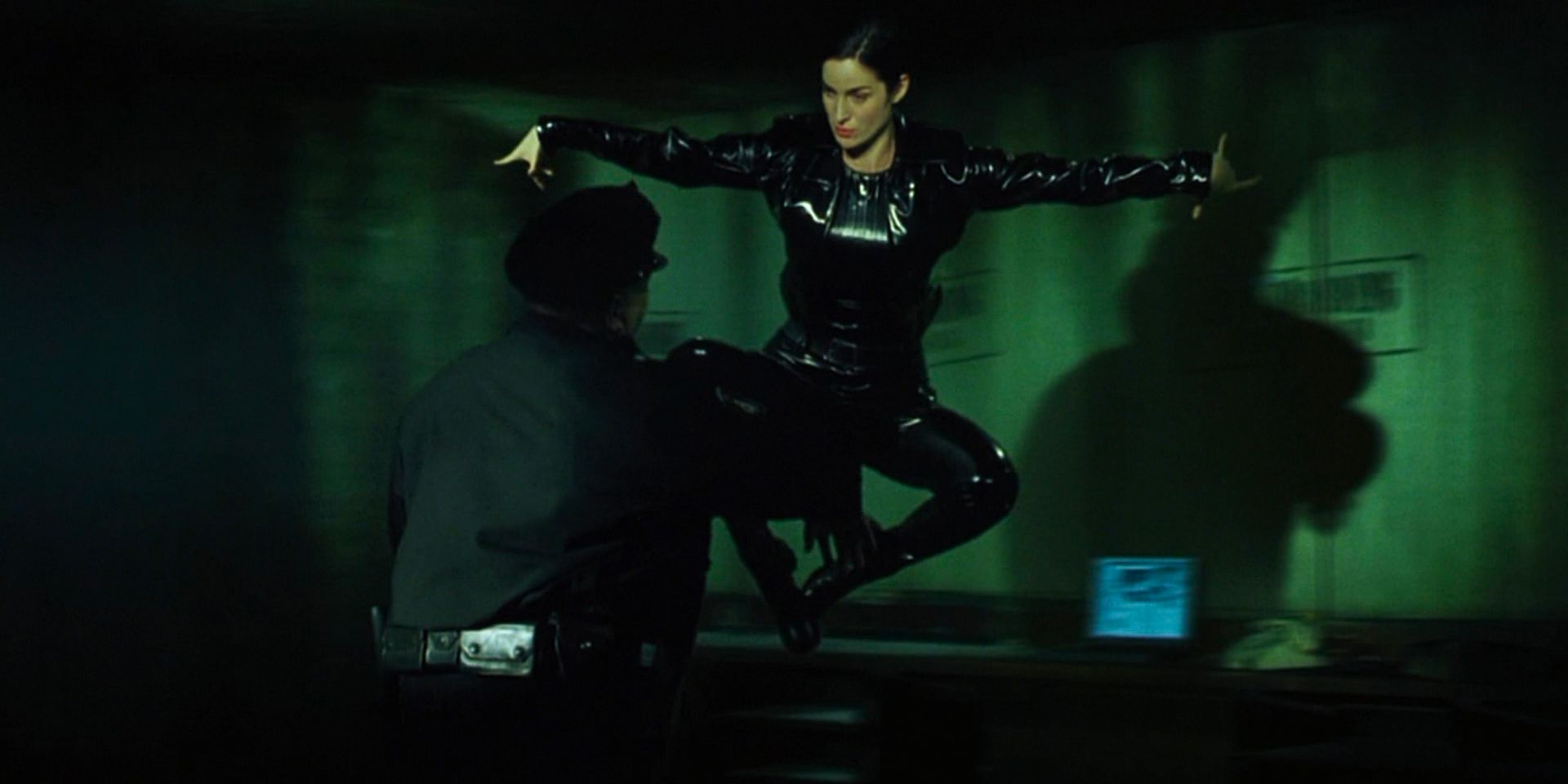 A woman in a leather outfit jumps and hovers in the air before fly-kicking a cop.