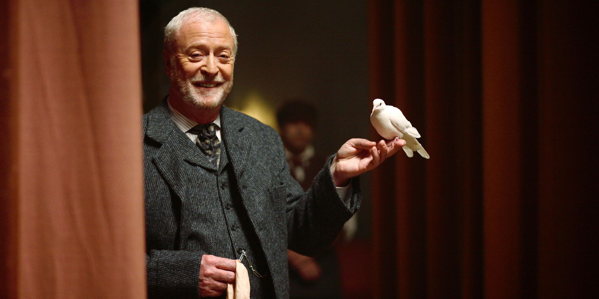 Michael Caine smiling with a bird perched on his hand in The Prestige