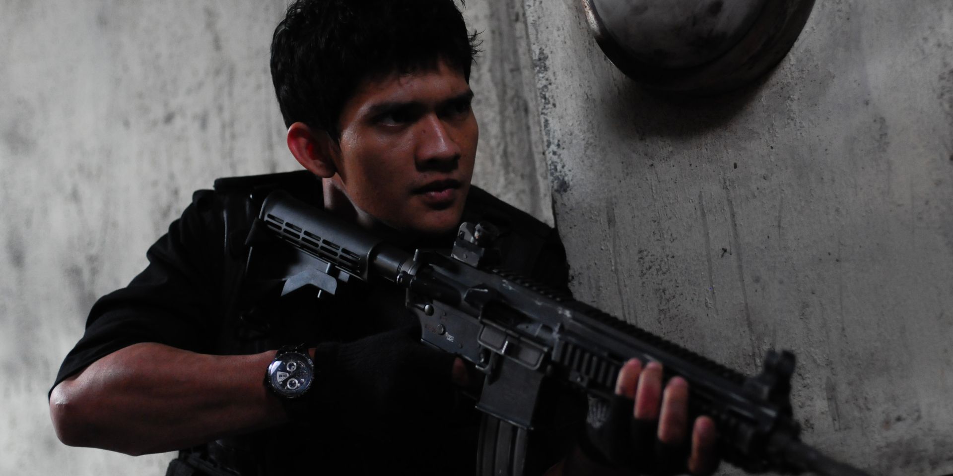 A rookie SWAT team member takes cover behind a wall with a machine gun in his hand.