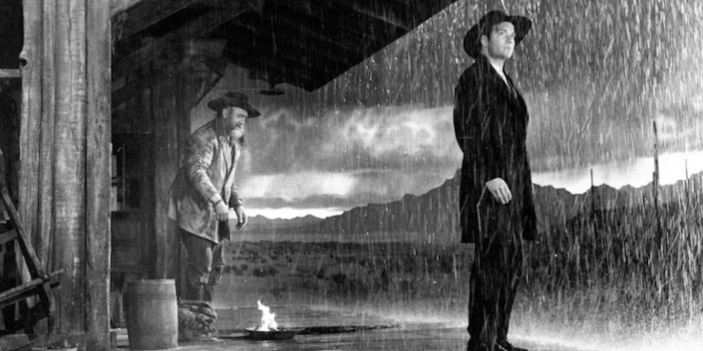 William Shatner de pie en el porche de un salón bajo la lluvia con Howard Da Silva detrás de él en The Outrage (1964)