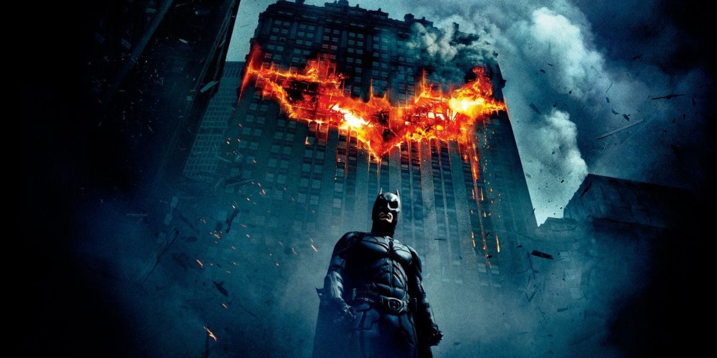 Batman está solo en los escombros de Gotham City con un símbolo de murciélago en llamas en el edificio detrás de él.