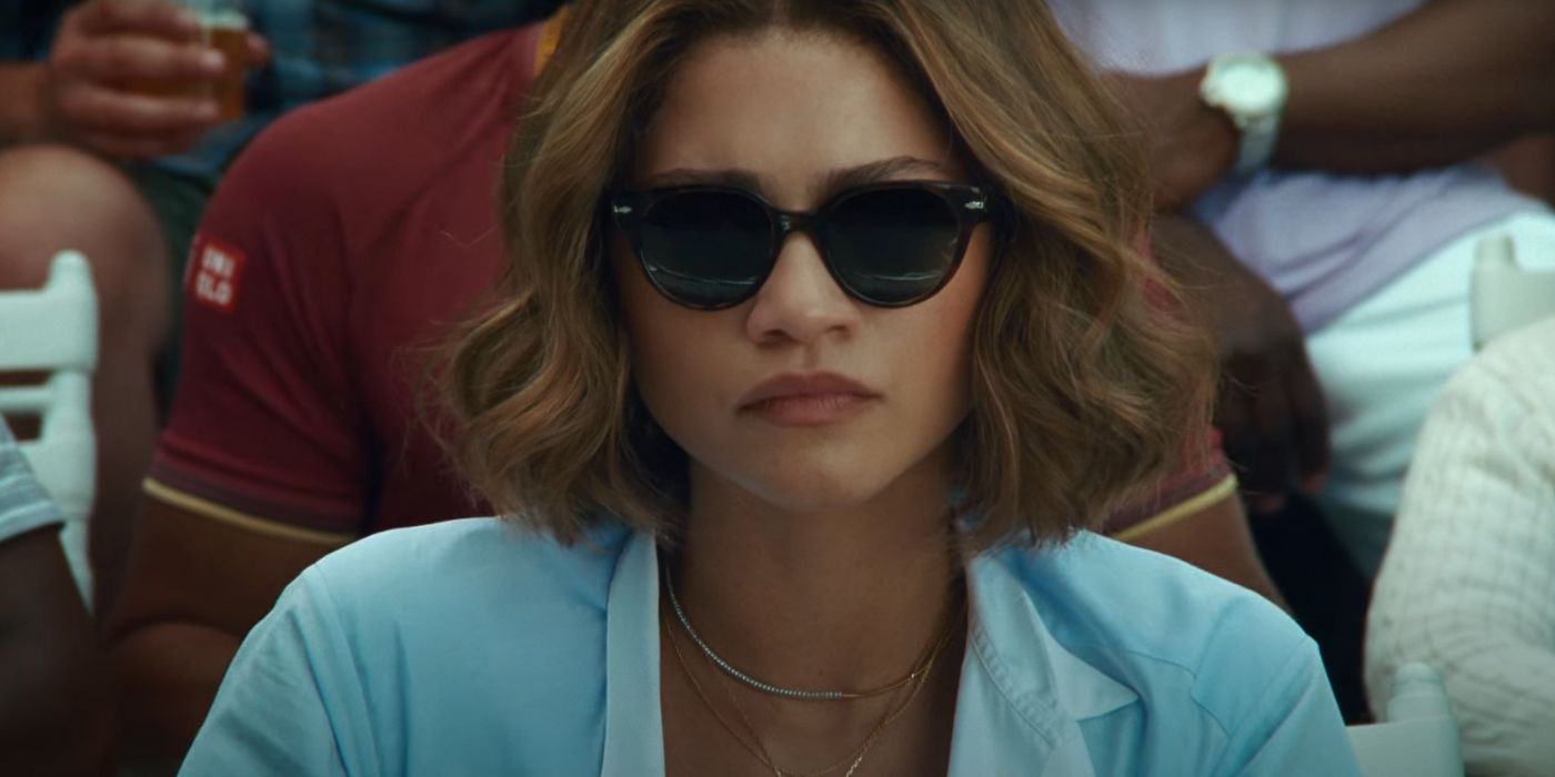 Zendaya as Tashi in Challengers​​​​​​​, wearing sunglasses while stoically watching a tennis match.