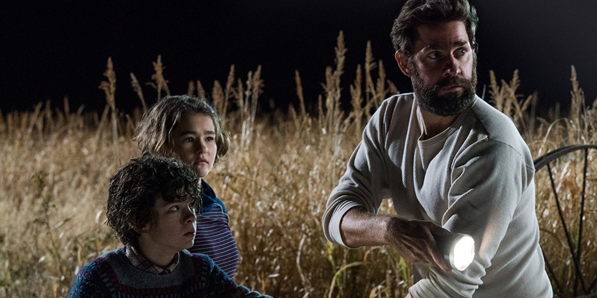 A father leads his two children through a field at night while trying not to make any noise. 