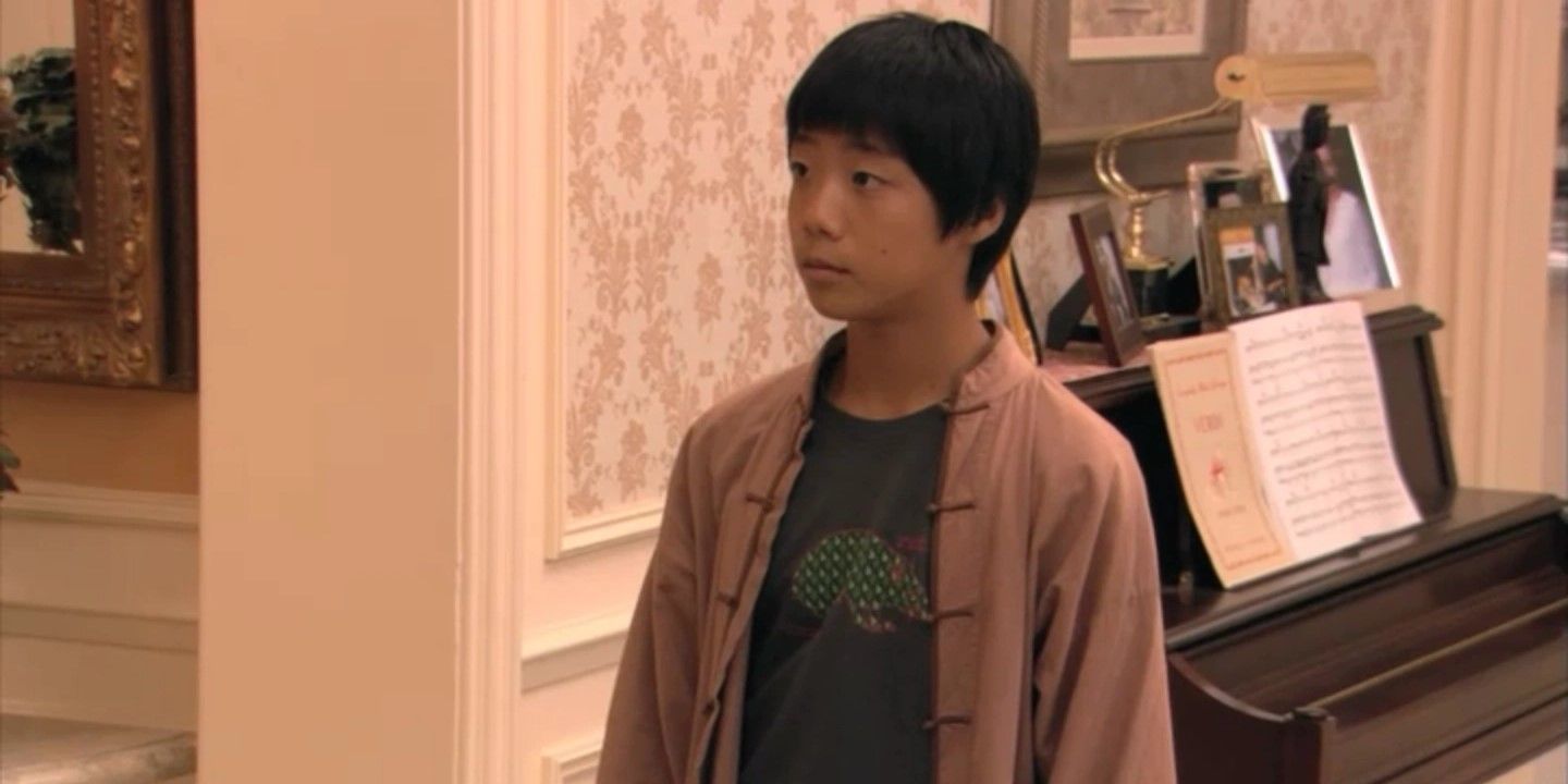 Still from 'Arrested Development': Annyong Bluth (Justin Lee) stands centre frame wearing a t-shirt with a mole design.