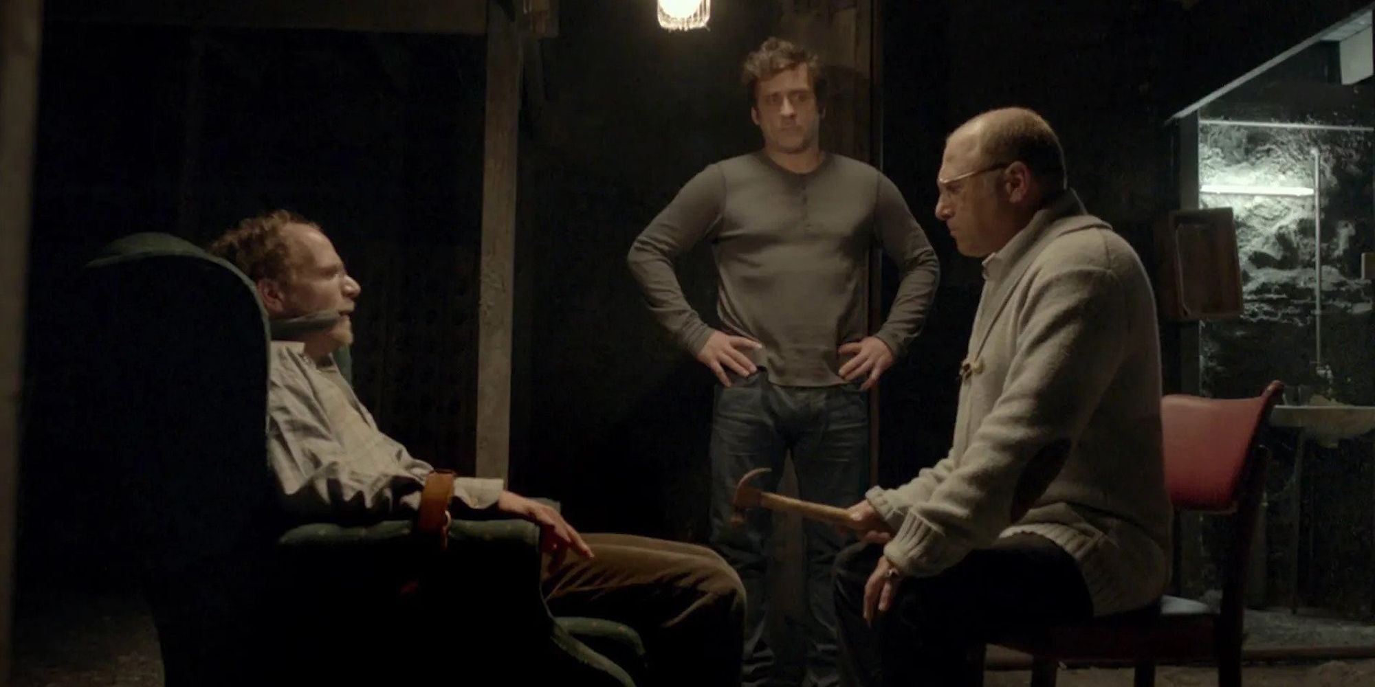 A man is tied to a chair while two other men threaten him with violence