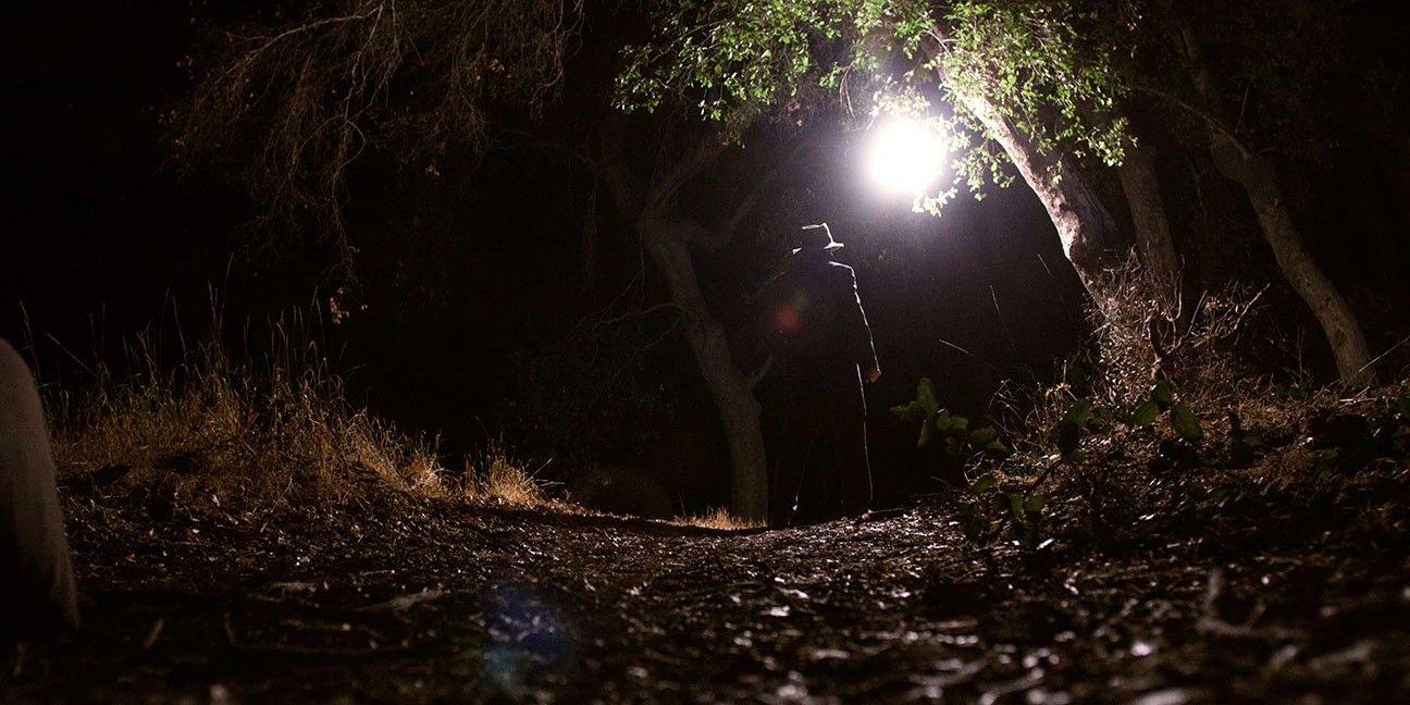 Image from 'Digging Up the Marrow' of a figure walking in the woods at night.