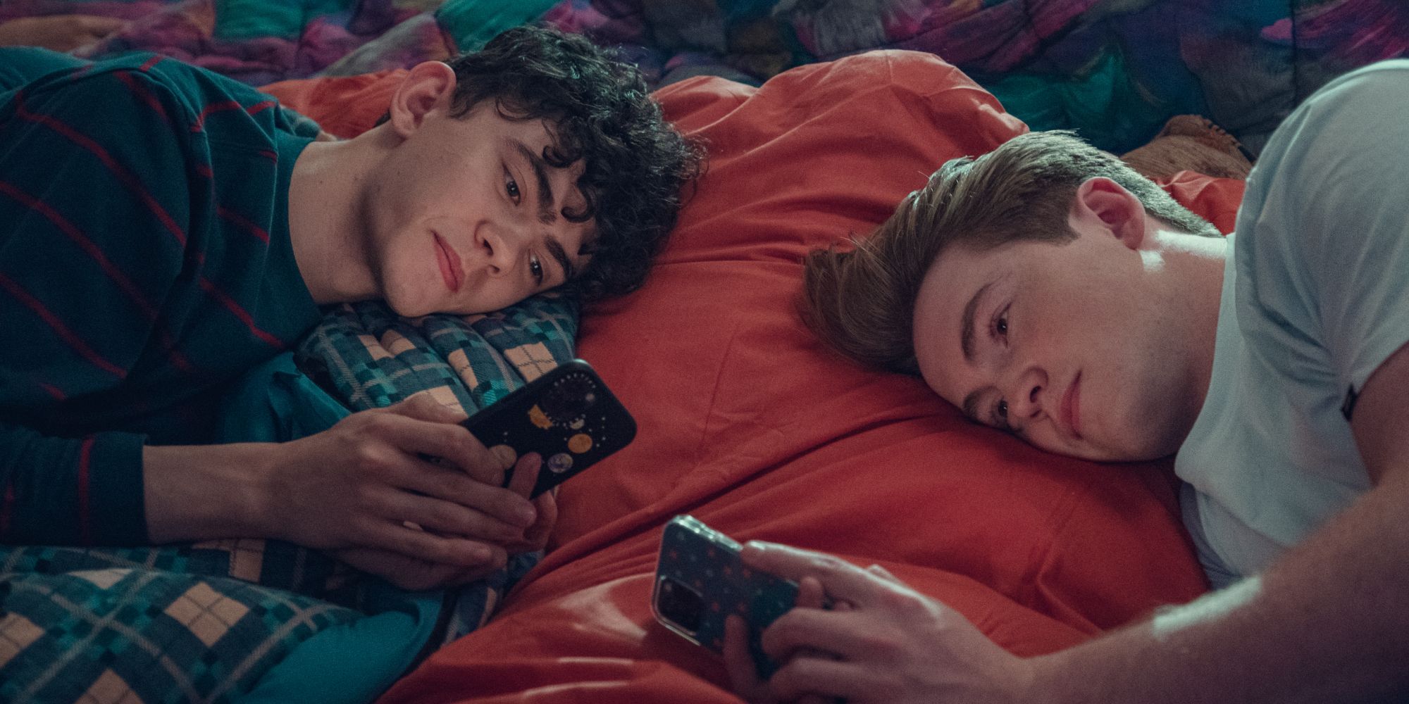 Joe Locke as Charlie and Kit Connor as Nick laying on their sides looking at their phones in Heartstopper Season 2