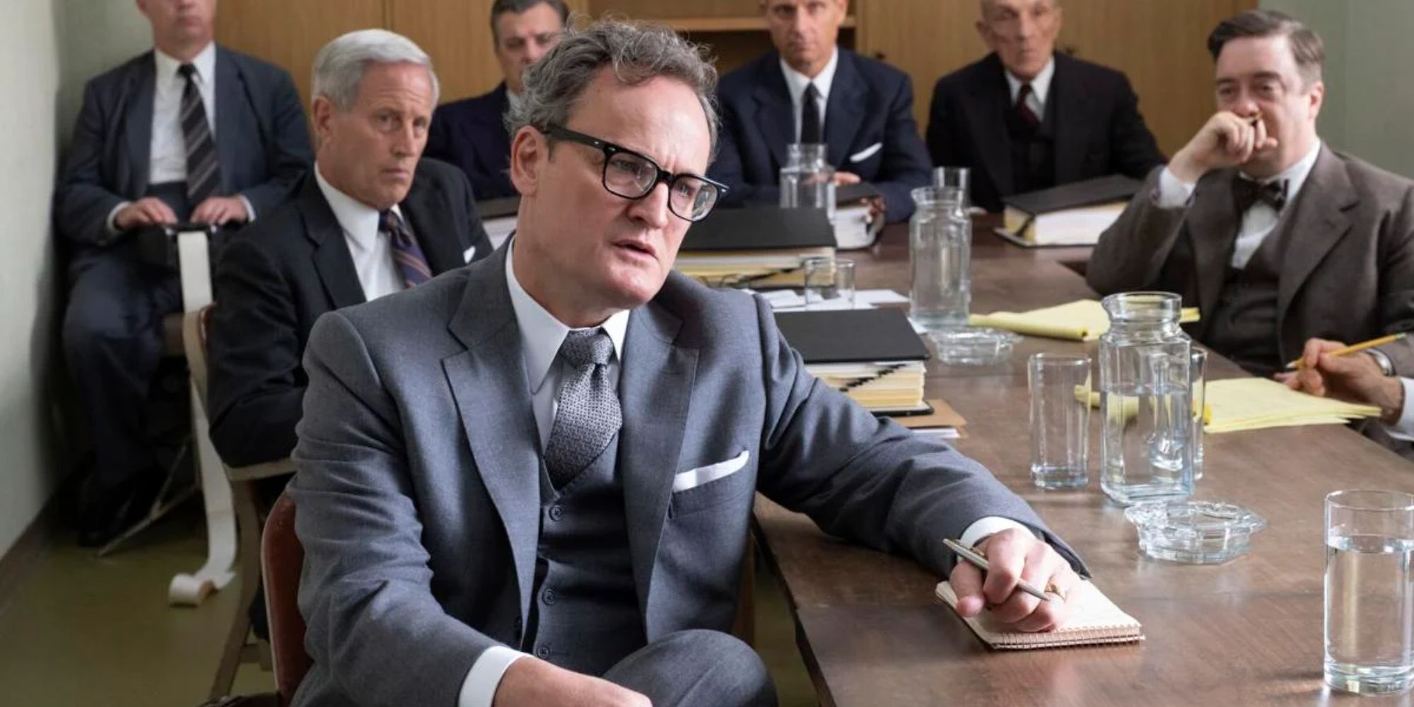 Jason Clarke as Roger Robb facing away from a group of men while taking notes in Oppenheimer