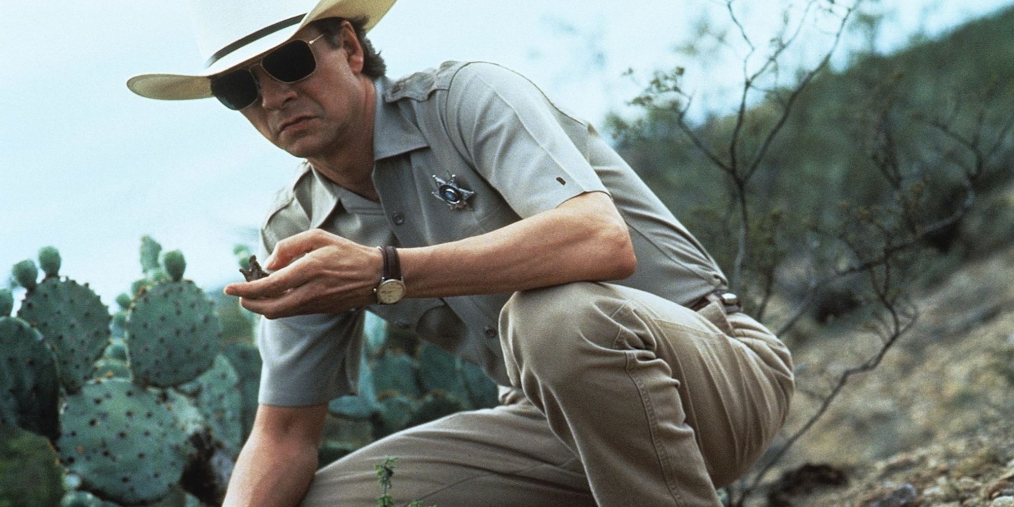 Chris Cooper as Sam Deeds crouching and examining something in his hand in Lone Star