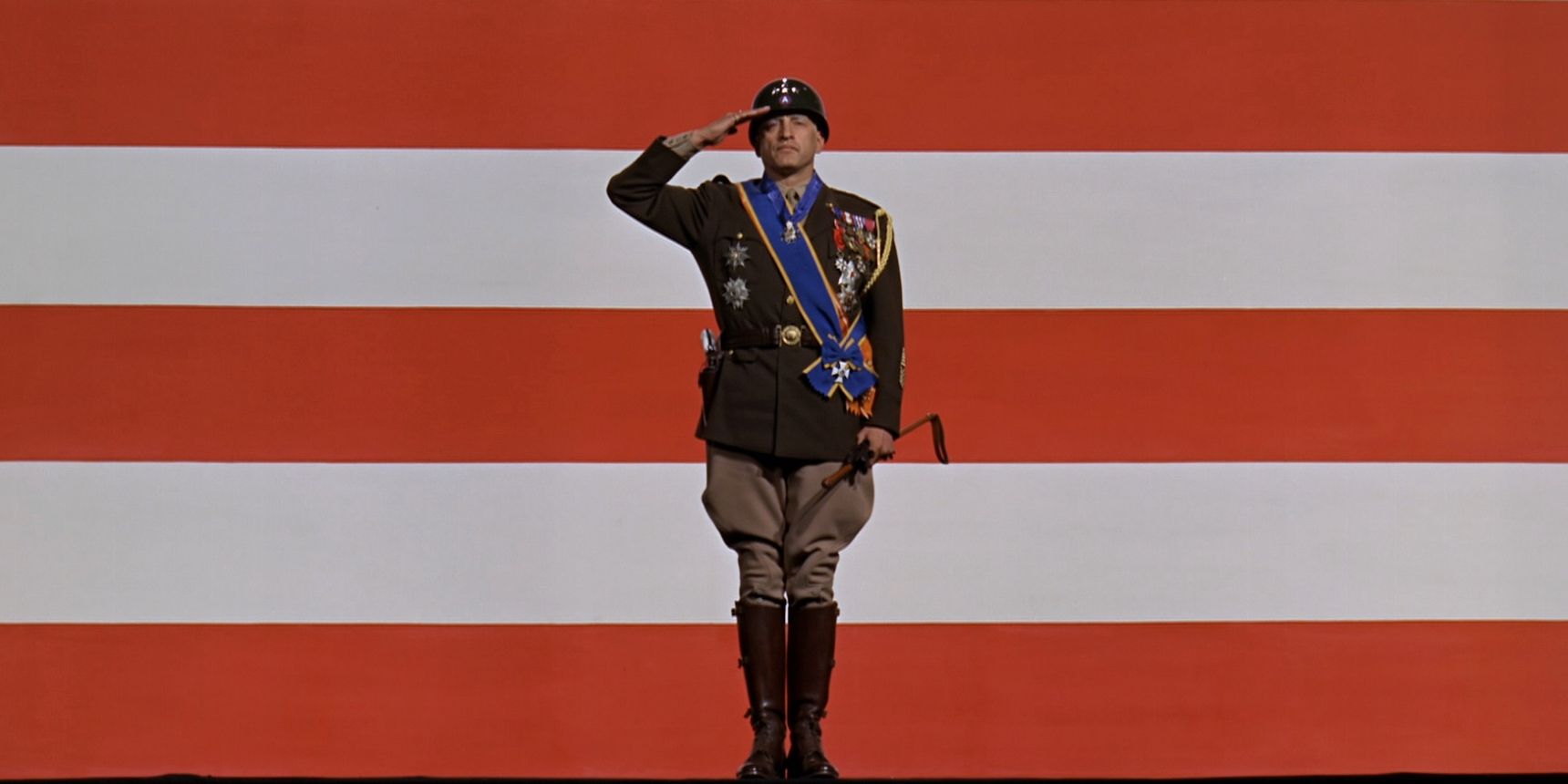 Le général Patton (George C. Scott) salue les troupes américaines en se tenant debout sur fond de drapeau américain.