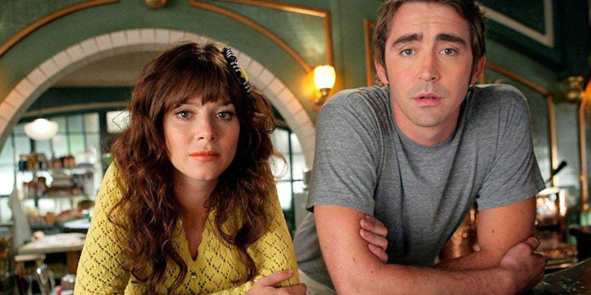 Anna Friel and Lee Pace in Pushing Daisies lean on a counter and look at the camera.