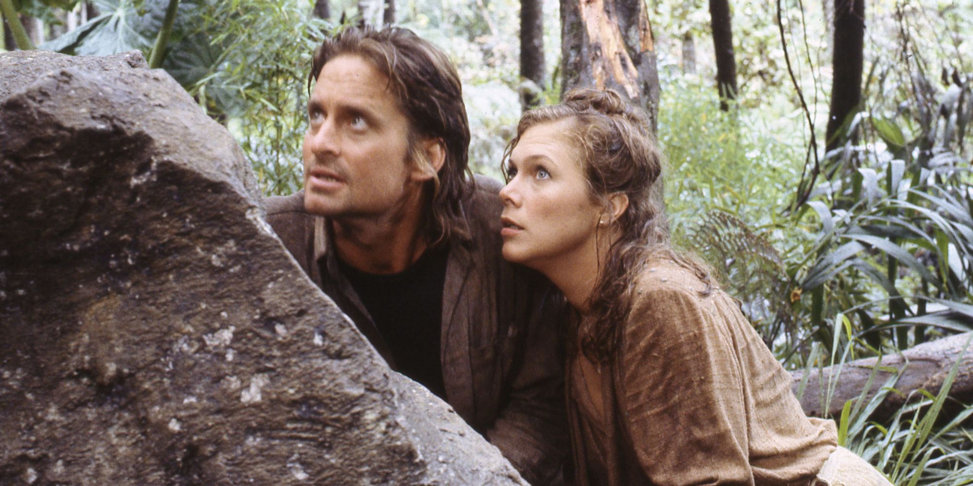 Jack and Joan looking to the distance from behind a large rock in in Romancing the Stone