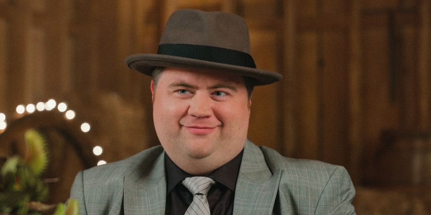 Travis (Paul Walter Hauser) wearing a hat and suit attends a wedding in The Afterparty Season 2